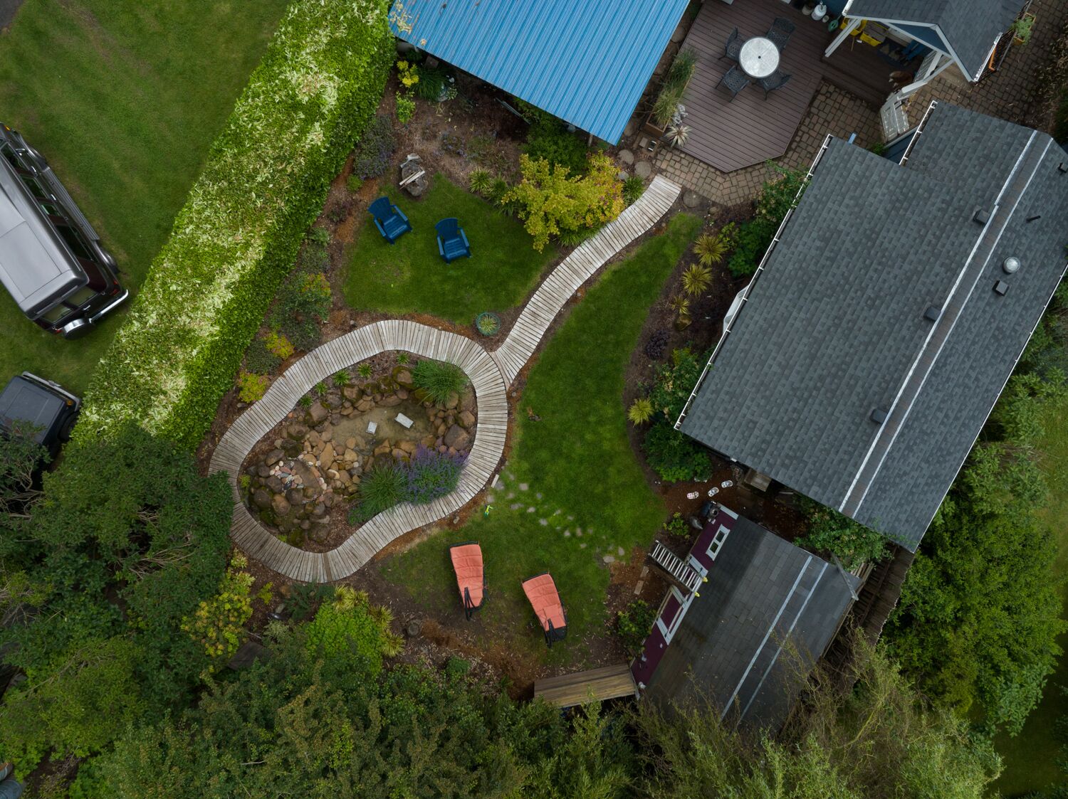 An aerial view of a residential property with a circular garden, a deck, and a blue-roofed building.