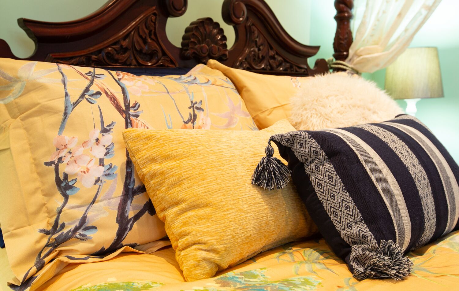 A bed with floral and striped pillows, a fluffy white pillow, and a wooden headboard.