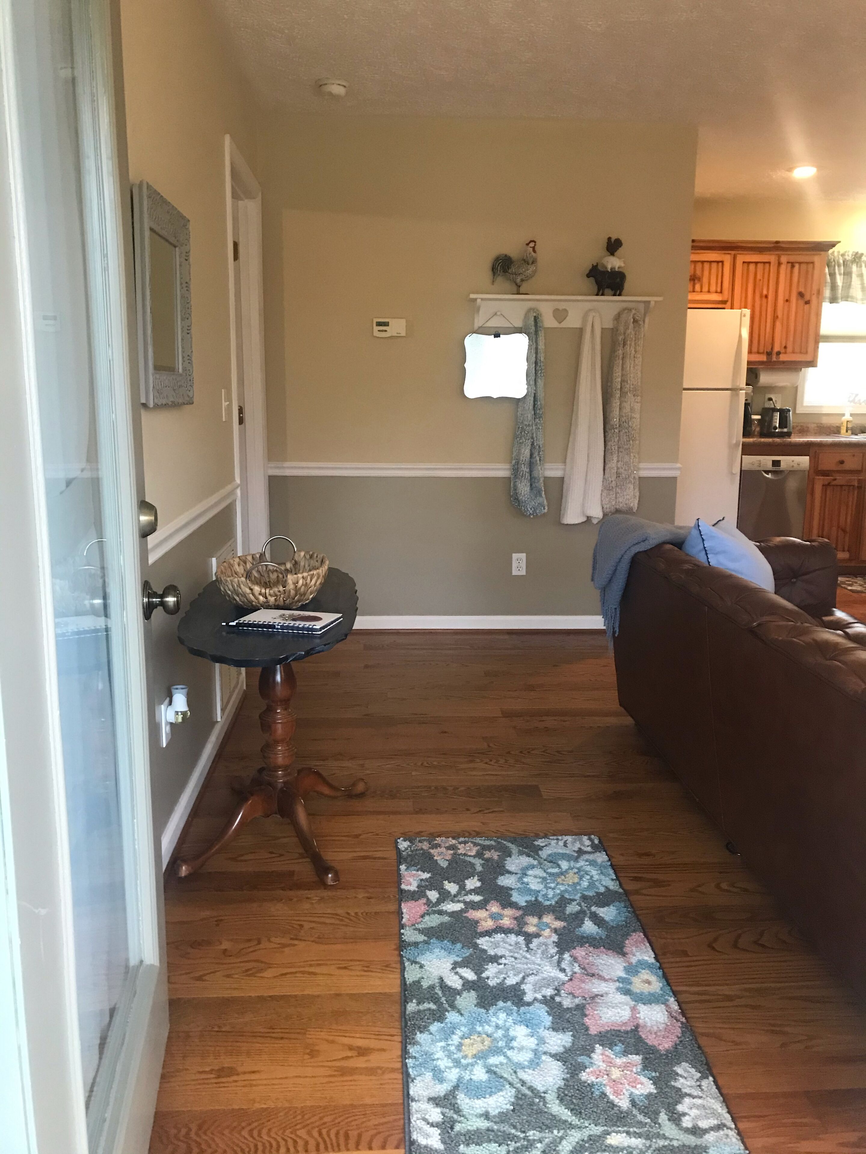 A cozy living room with a brown leather couch, a small round table with a basket, and a floral area rug.
