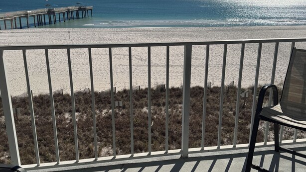 Une vue sur la plage depuis un balcon doté d’une balustrade, agrémenté d’un tapis à motifs et d’une chaise.