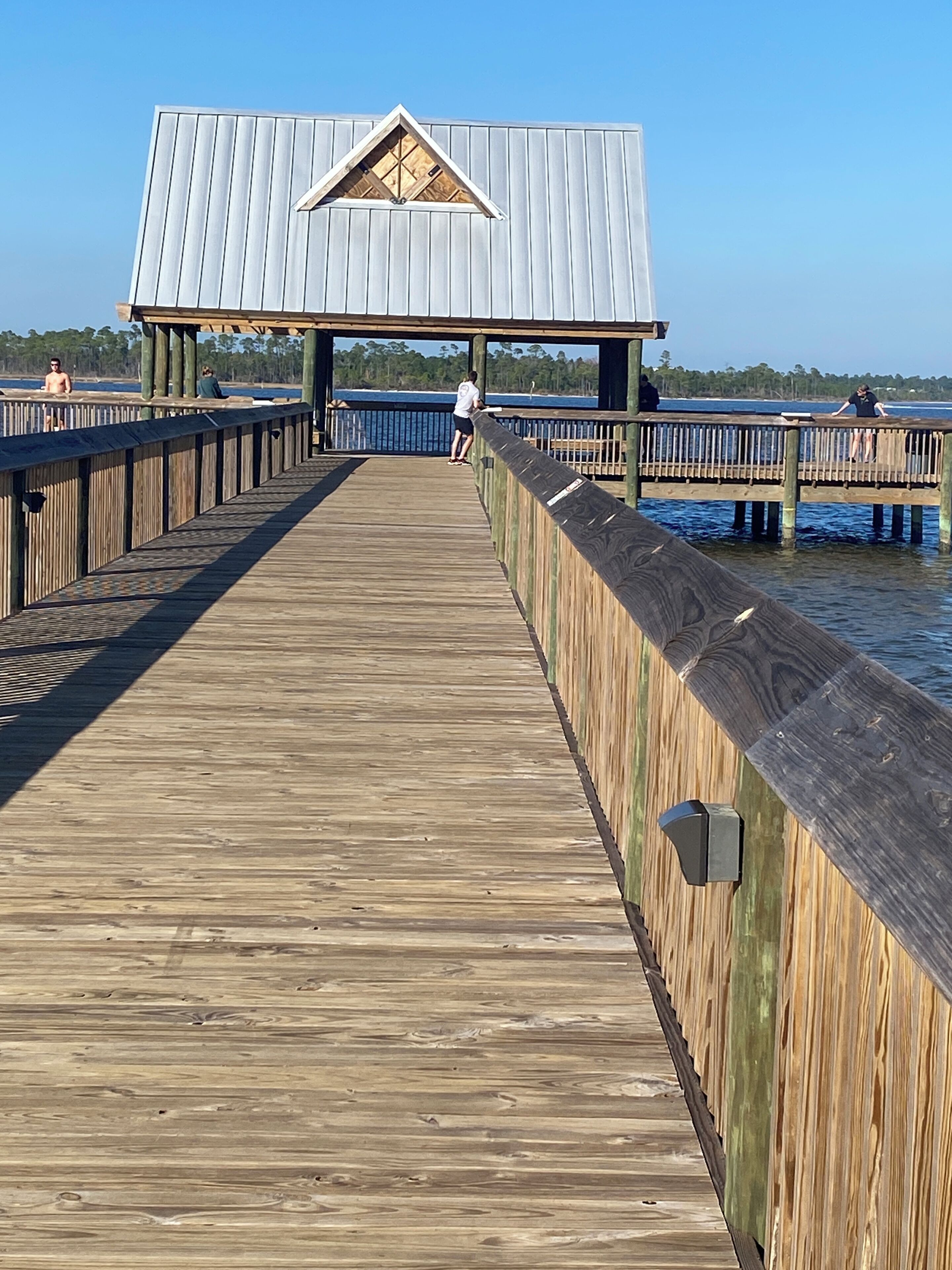 Un muelle de madera que conduce a una estructura con techo metálico y un ventanal triangular.