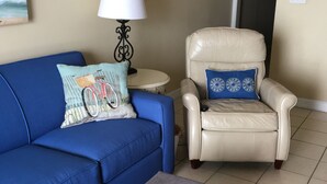Un salon avec un canapé bleu, un fauteuil blanc, une petite table ronde avec une lampe et un tapis coloré.