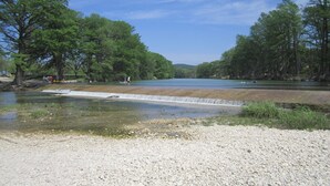 A river with a dam, surrounded by trees and a clear sky. - One and a half miles from the Frio River! The stars at night are big and bright! (Leakey)