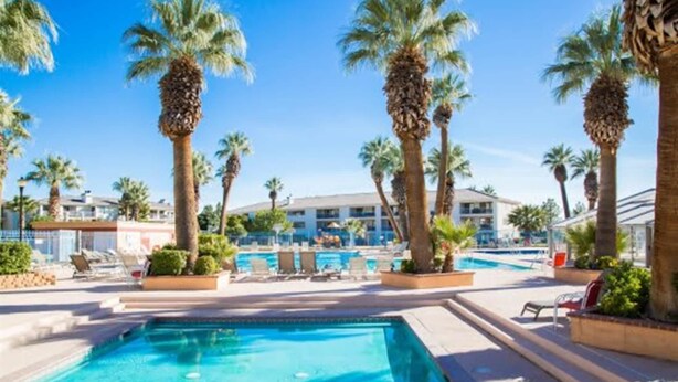 Ein Poolbereich mit mehreren Pools, Palmen und einem Gebäude im Hintergrund.