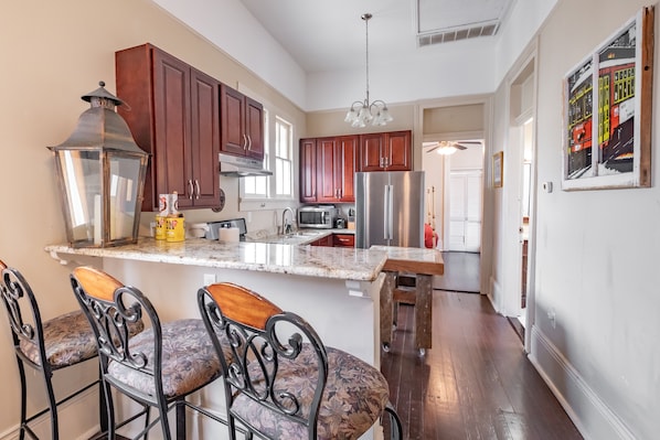 A kitchen with wooden cabinets, a stainless steel refrigerator, a bar area with metal chairs, and a hanging light fixture.