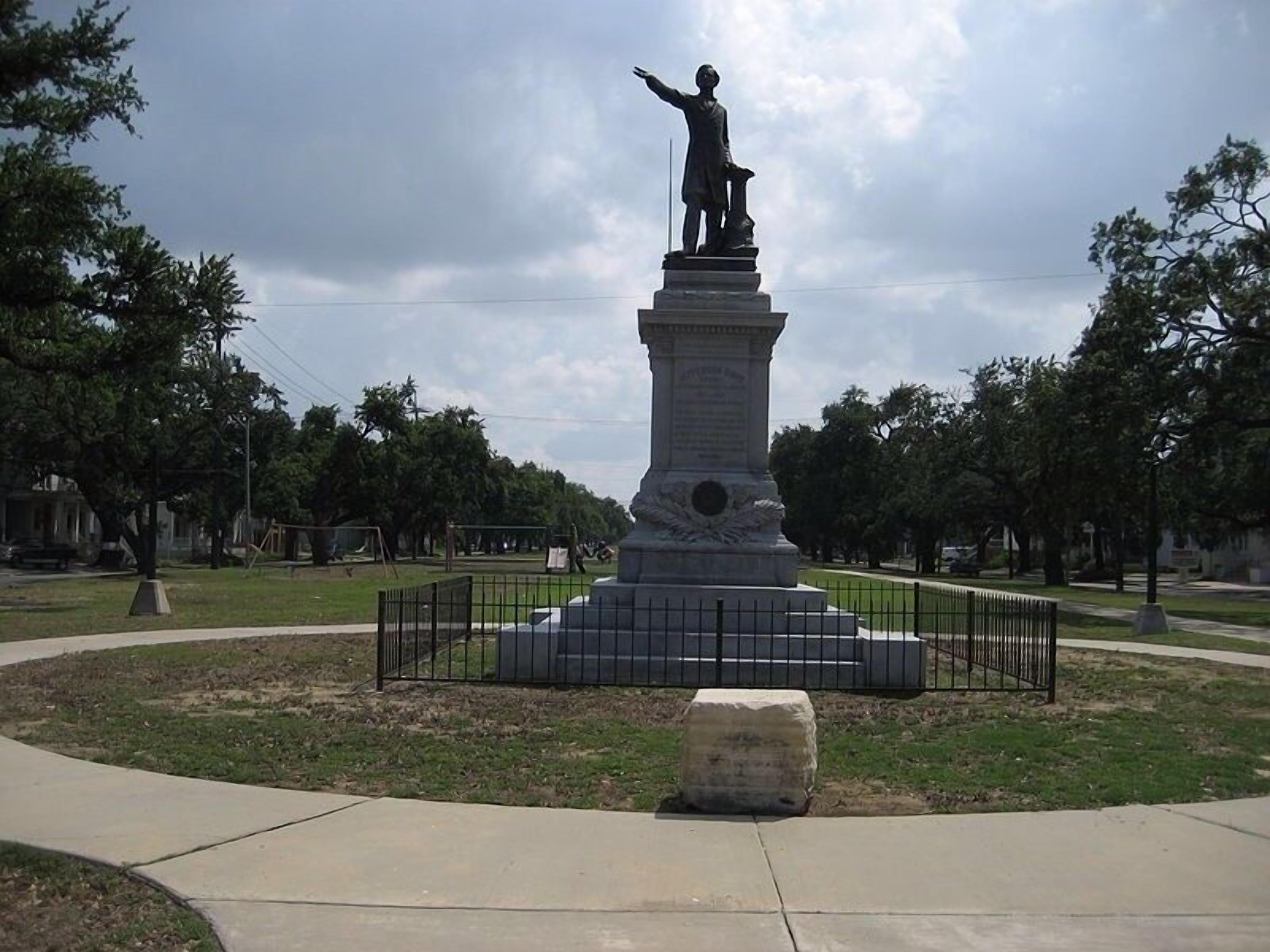 A statue in a park with a paved walkway and trees.