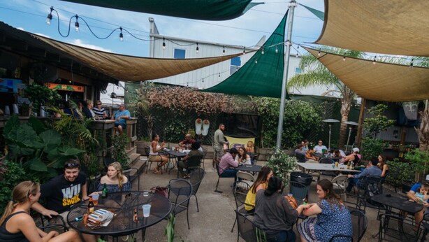 Un espace extérieur aménagé en terrasse, avec des tables et des chaises rondes, entouré de verdure et ombragé par de grands auvents en tissu.