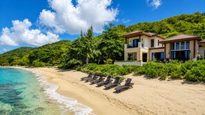 A beachfront property with a pool, lounge chairs, and a two-story building. - Living Waters  Luxury Beachfront Estate (Roatan)