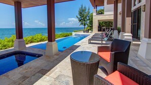 Zona de piscina con sillones de descanso y una mesa, con vista al mar.