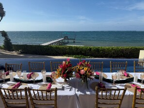 Une table à manger avec des chaises, une vue sur la mer et une jetée en arrière-plan.