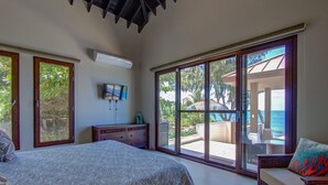 Un dormitorio con una cama grande, televisor y puerta corrediza de vidrio que da a un balcón con vista al océano.