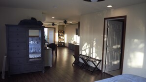 Ein Schlafzimmer mit einem Bett, einem Schminktisch und einem Schreibtisch mit Stuhl. Eine Tür und ein Deckenventilator sind vorhanden.