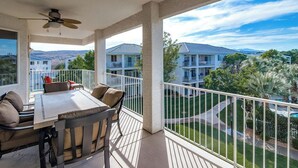 Un balcone con tavolo e sedie, una ventola a soffitto e vista su abitazioni vicine e una piscina.