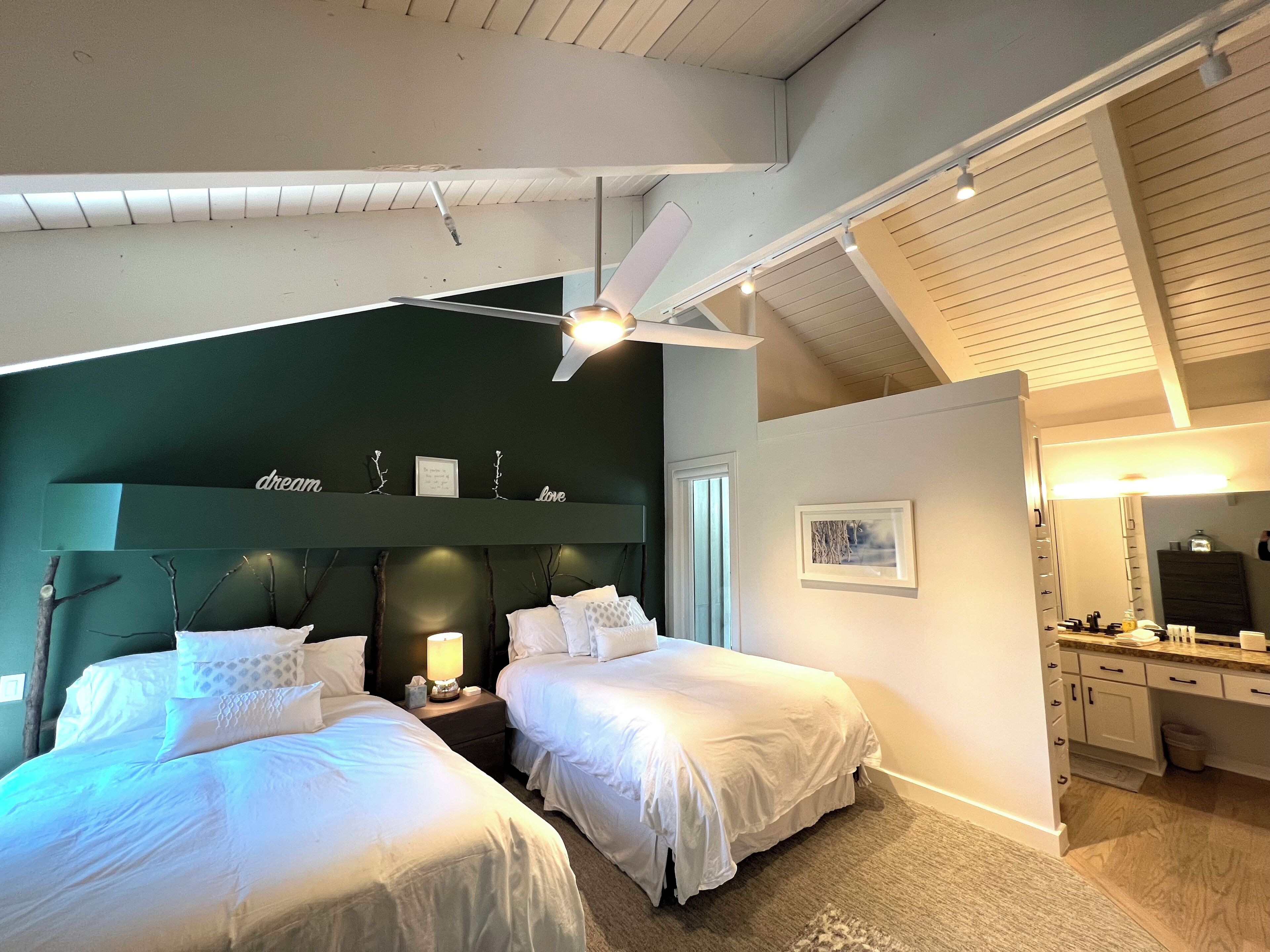 A bedroom with two beds, a ceiling fan, and a nightstand with a lamp.