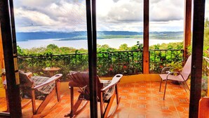 Een balkon met uitzicht op een meer en bergen, ingericht met stoelen en een tafel.