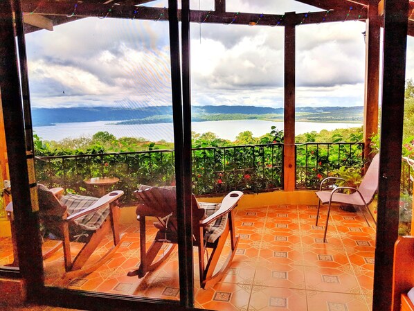 A balcony with a view of a lake and mountains, furnished with chairs and a table.