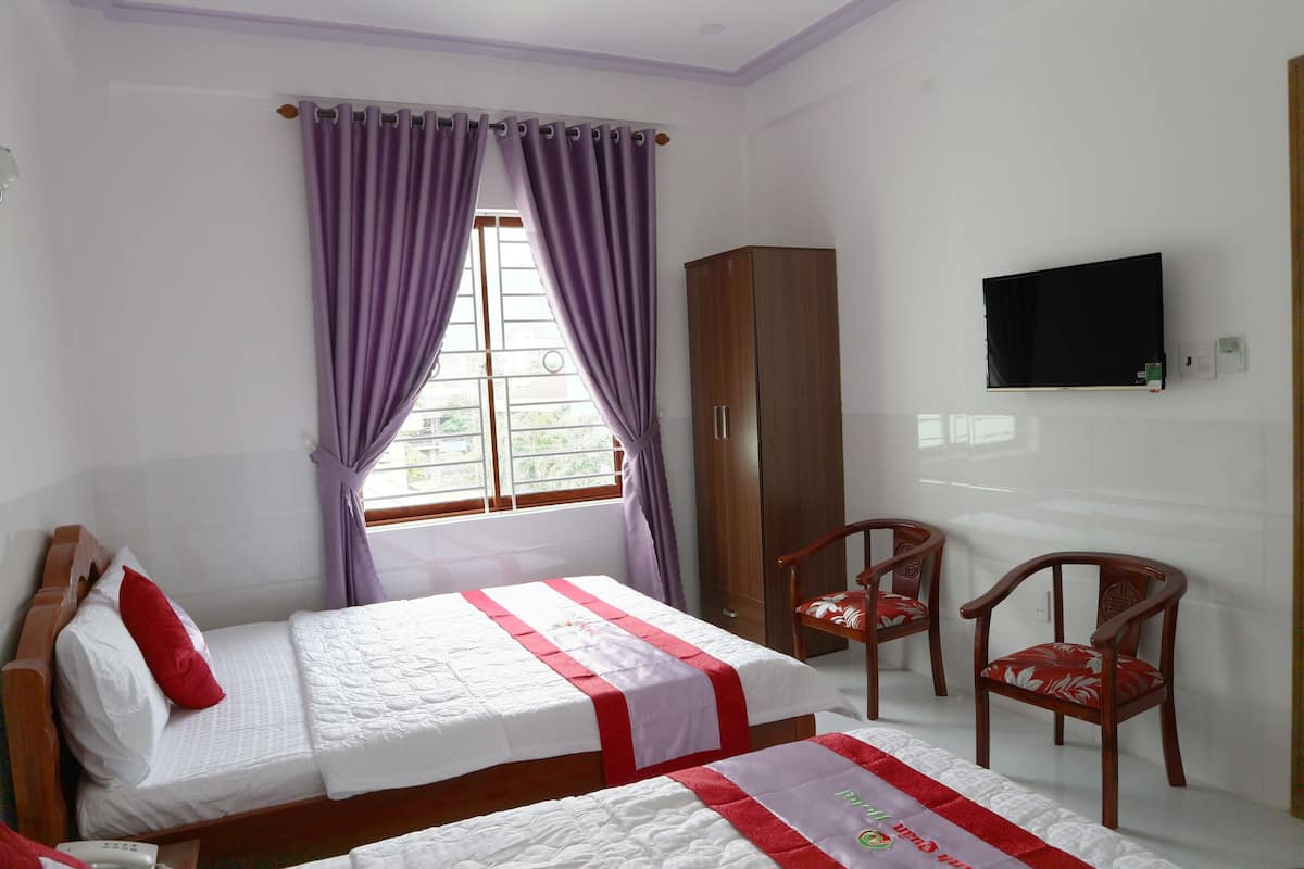 A hotel room with two beds, a wardrobe, a TV, and two chairs.