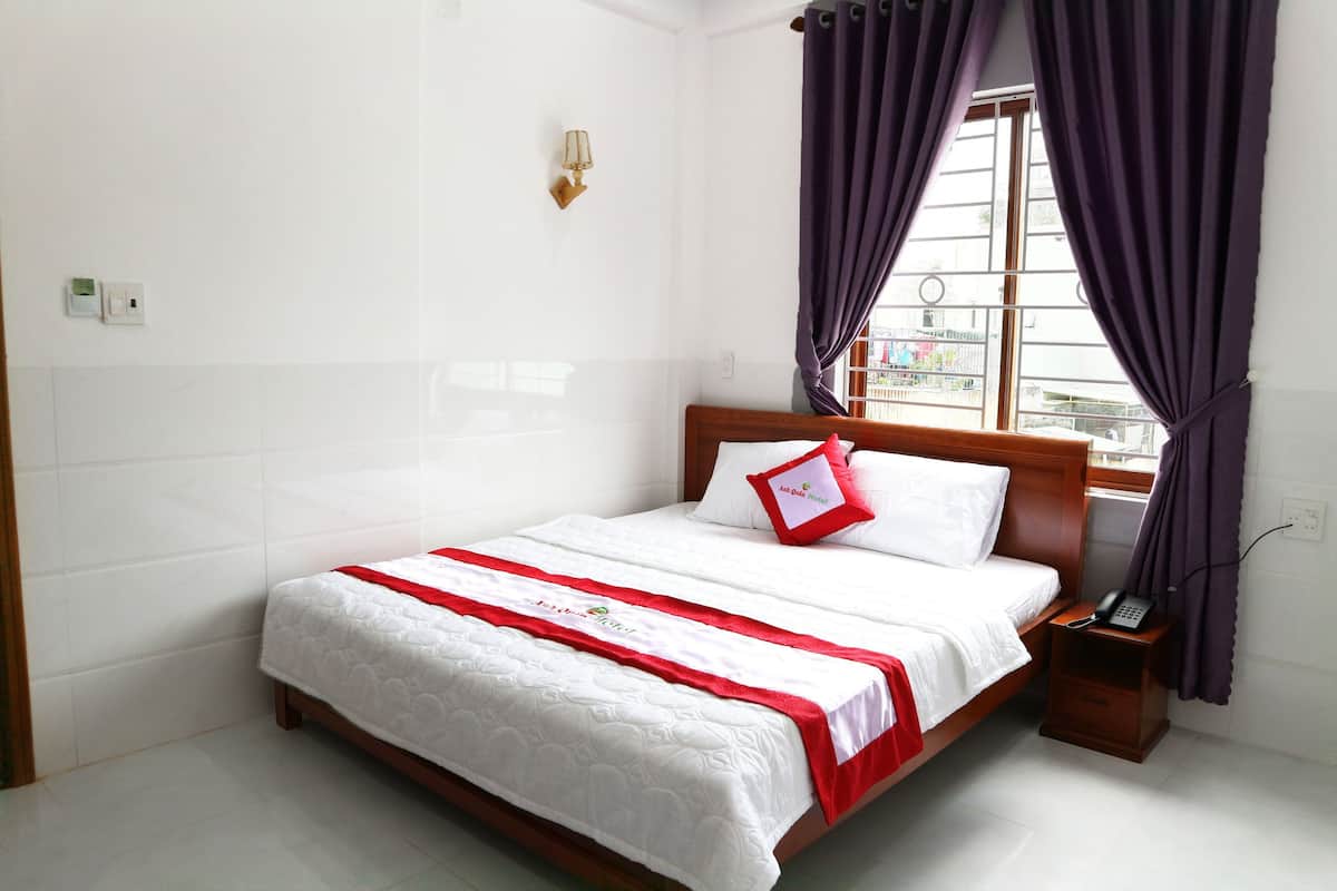 A neatly made bed with a red and white bedspread, a wooden headboard, and a bedside table with a phone.