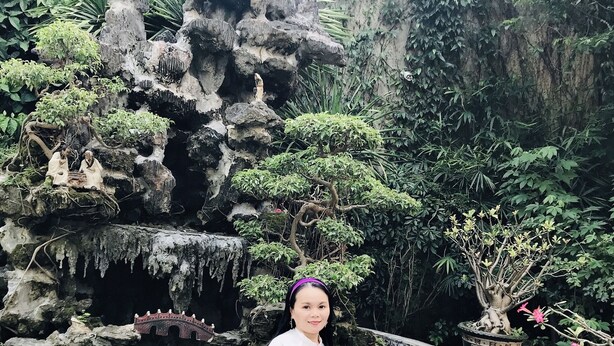 A woman sitting by a rock formation with a small bridge and a pond. - Anh Quan Hotel (Quy Nhon Nam)