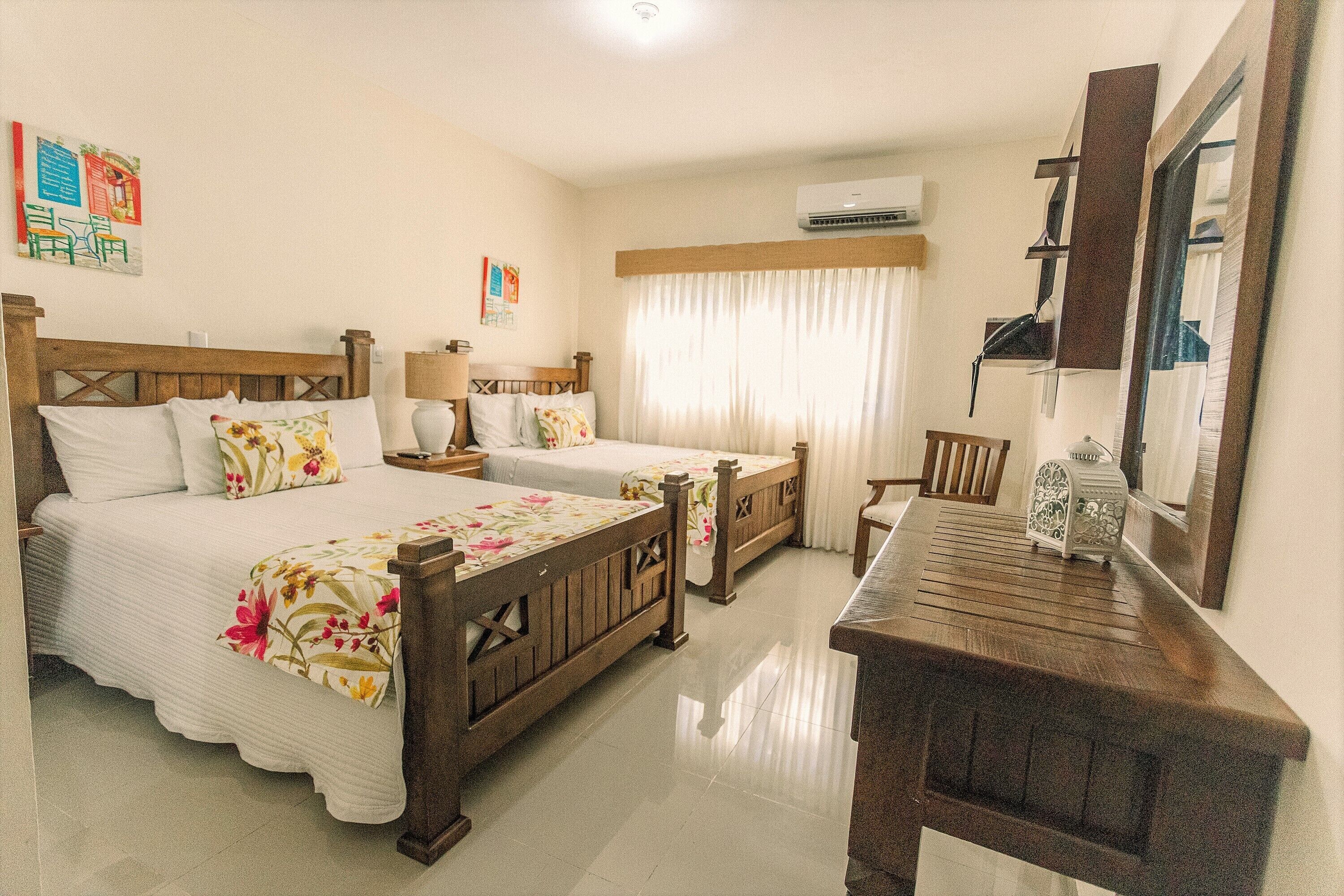 A hotel room with two wooden beds, a wooden desk, a chair, a lamp, and a mirror.