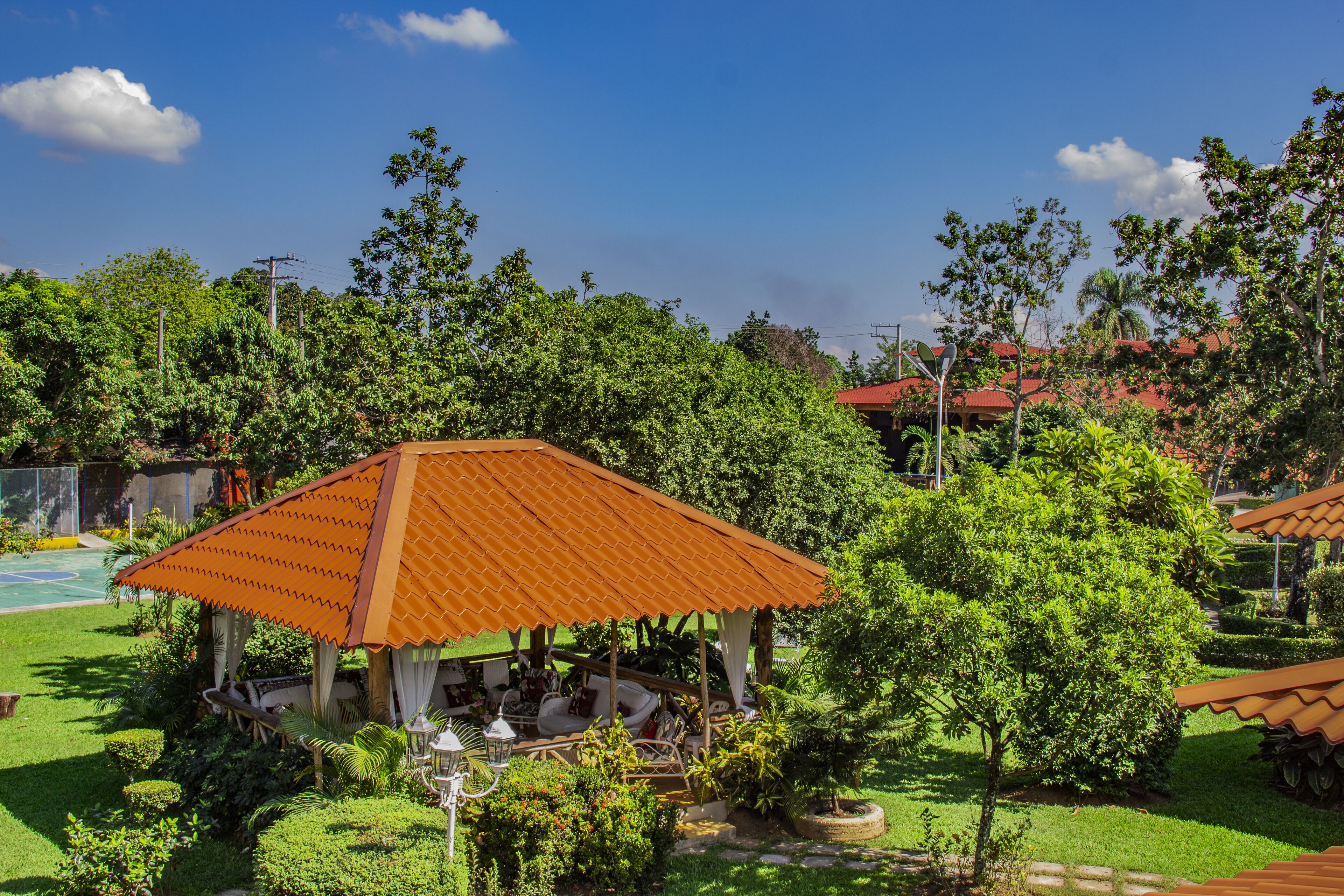 A gazebo with a tiled roof surrounded by lush greenery and a well-maintained lawn.