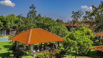 A gazebo with a tiled roof surrounded by lush greenery and a well-maintained lawn.