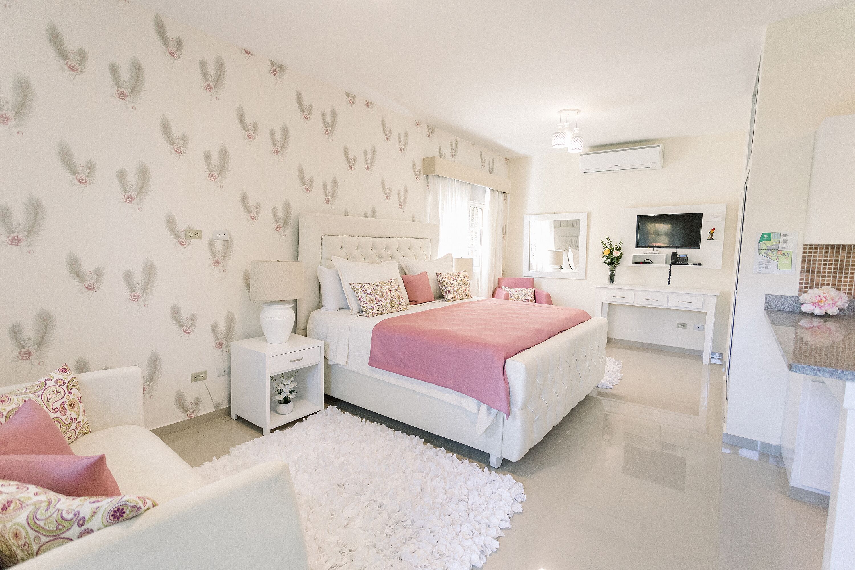 A bedroom with a large bed, bedside tables, a dresser, a TV, and a bathroom with a mirror and sink.