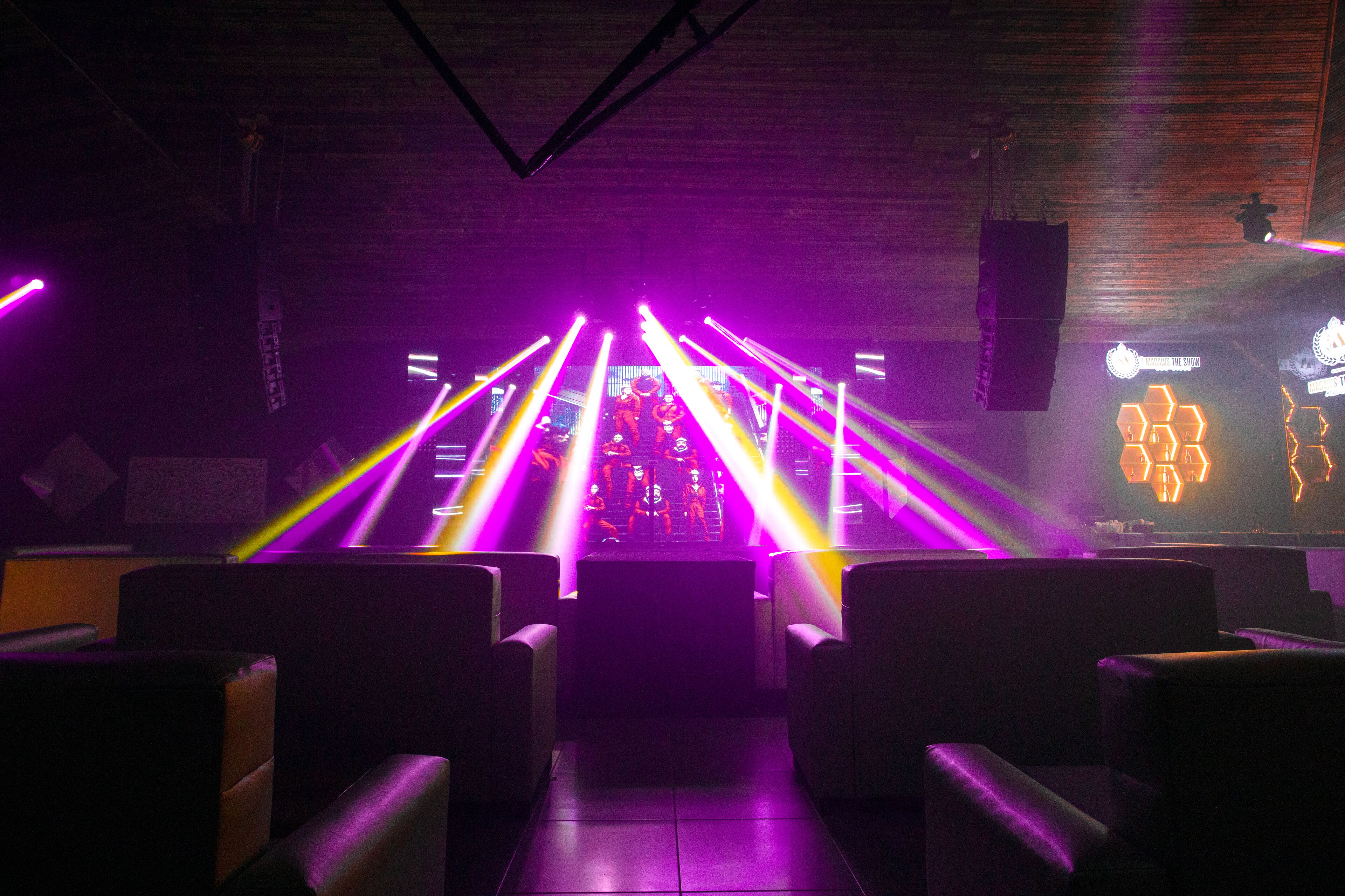 A dimly lit room with rows of seats facing a stage with colorful stage lighting.