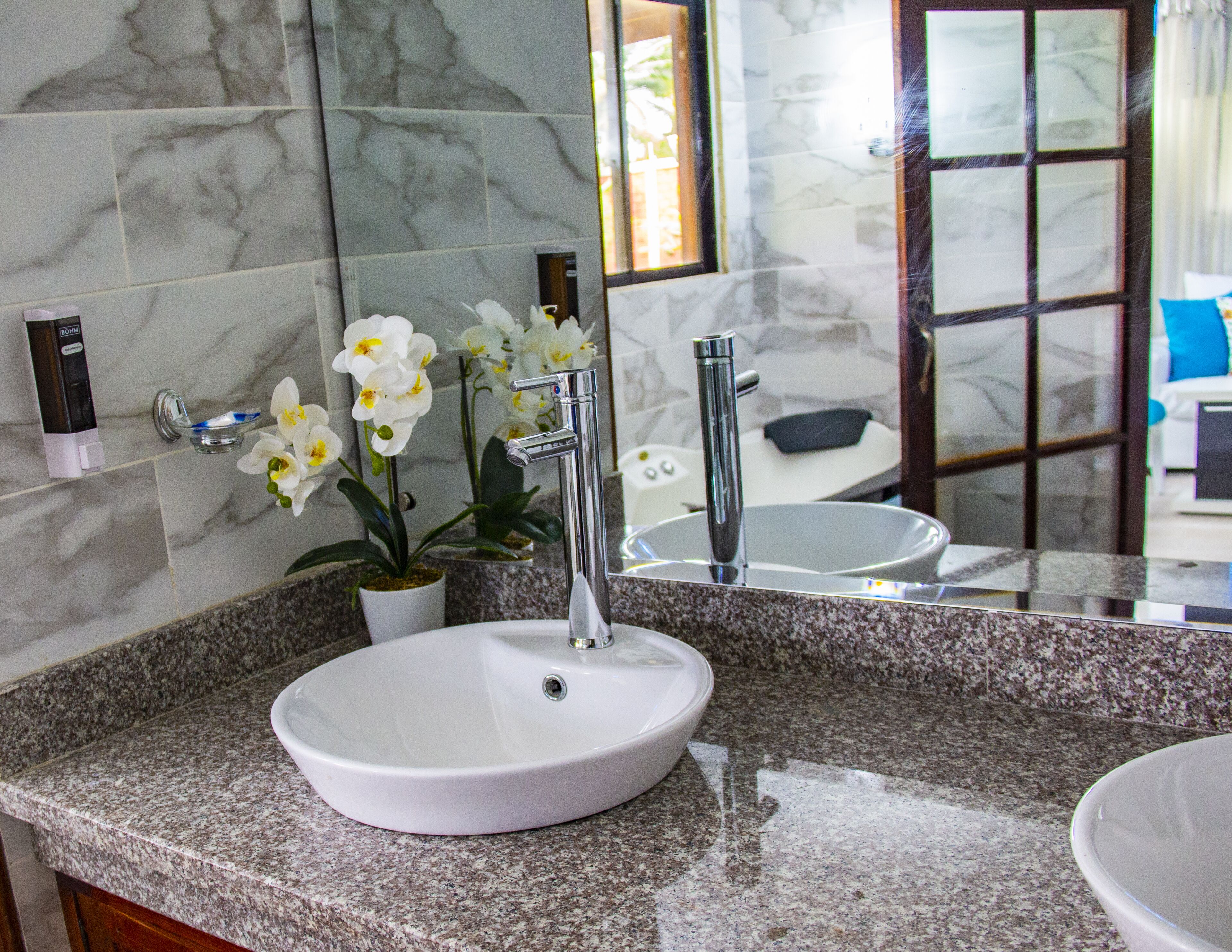 A bathroom with a white sink, a modern faucet, and a potted orchid.
