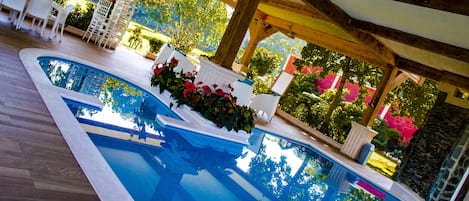 Una piscina interior con suelo de madera, sillas blancas y plantas en macetas.