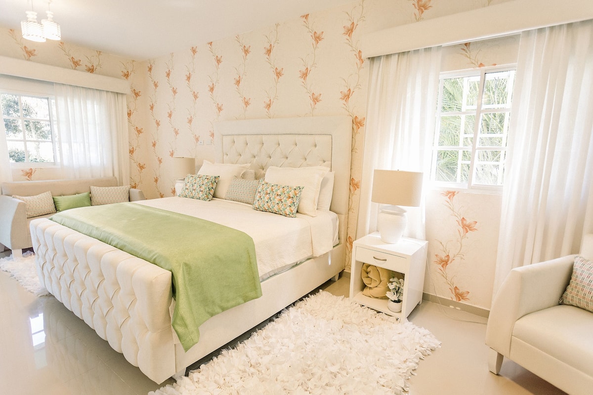 A spacious bedroom with a large bed, a bedside table, and a chair.