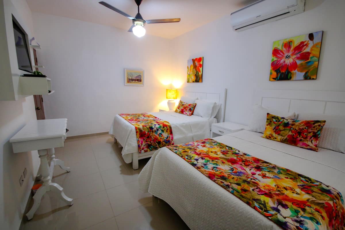 A bedroom with two beds, a bedside table, a nightstand, a ceiling fan, and a wall-mounted air conditioner.