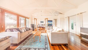 A spacious living room with a large window, a sofa, a coffee table, and a TV. - Outlook Hill Vineyard Cottages (Tarrawarra)