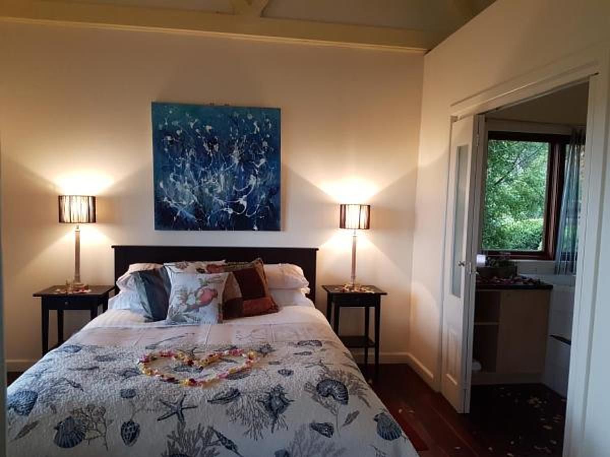 A bedroom with a bed, two bedside lamps, a painting on the wall, and a window with a view of greenery.