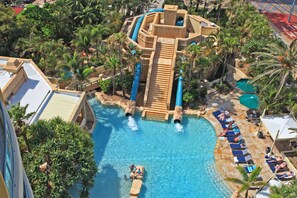 Luchtbeeld van een resort met een groot zwembad, glijbanen en loungegedeeltes, omgeven door palmbomen.