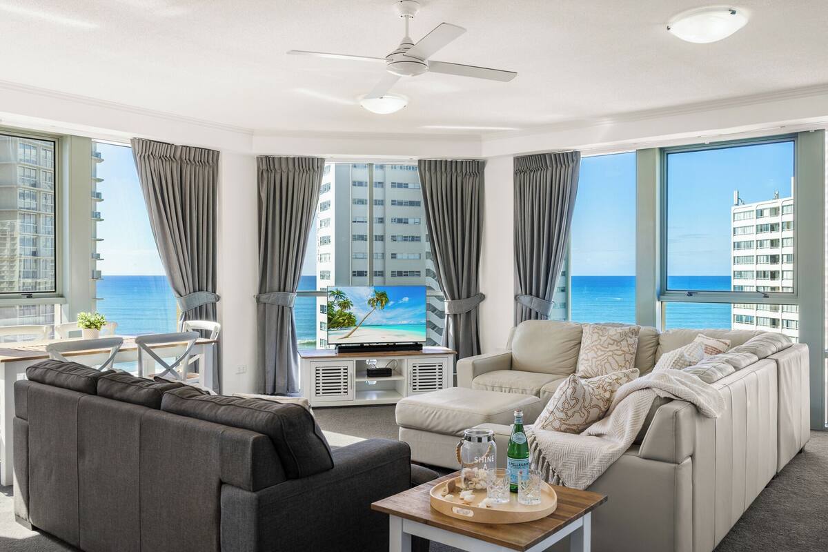 A modern living room with a sofa, armchair, and a TV displaying a beach scene.