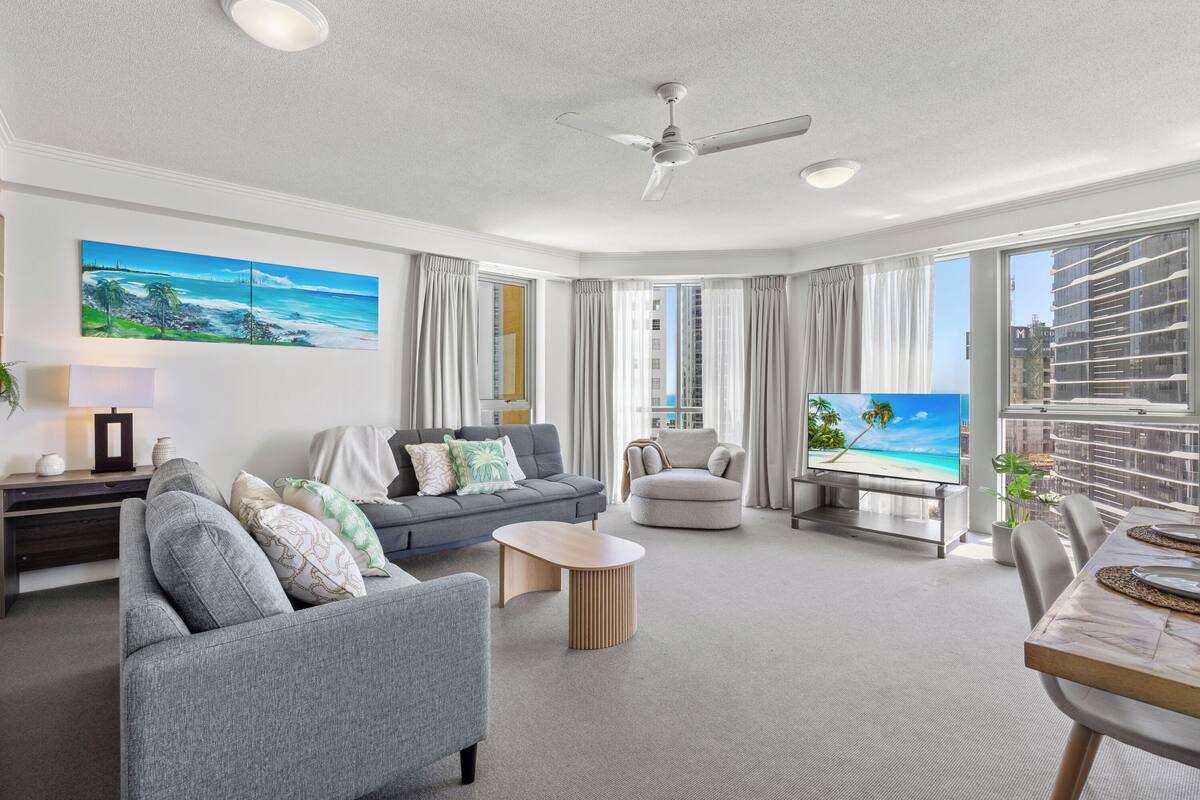 A modern living room with a grey sofa, a round armchair, a coffee table, and a TV displaying a beach scene.