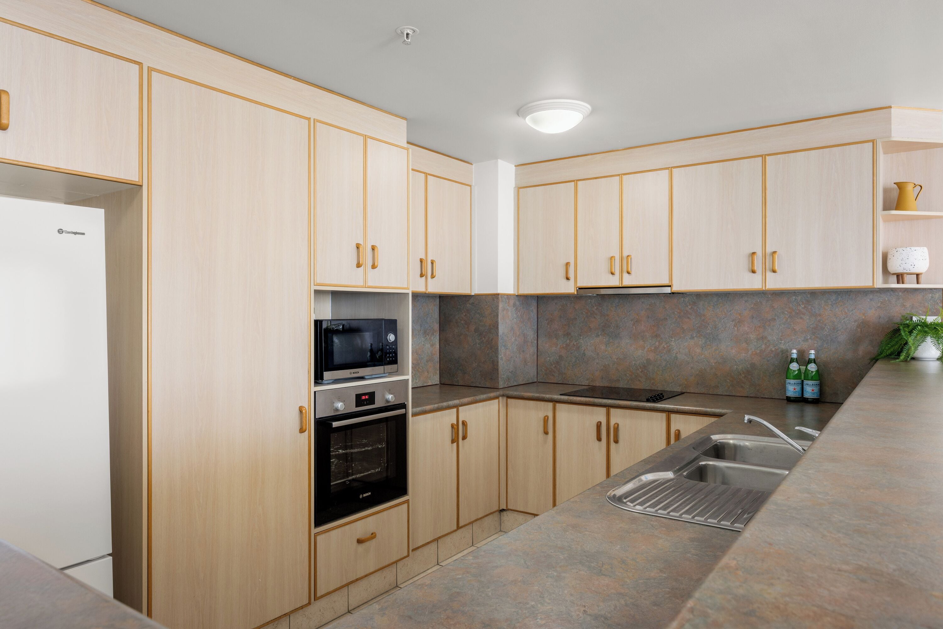 Une cuisine moderne avec des meubles en bois clair, des appareils en acier inoxydable et un plan de travail en granit.