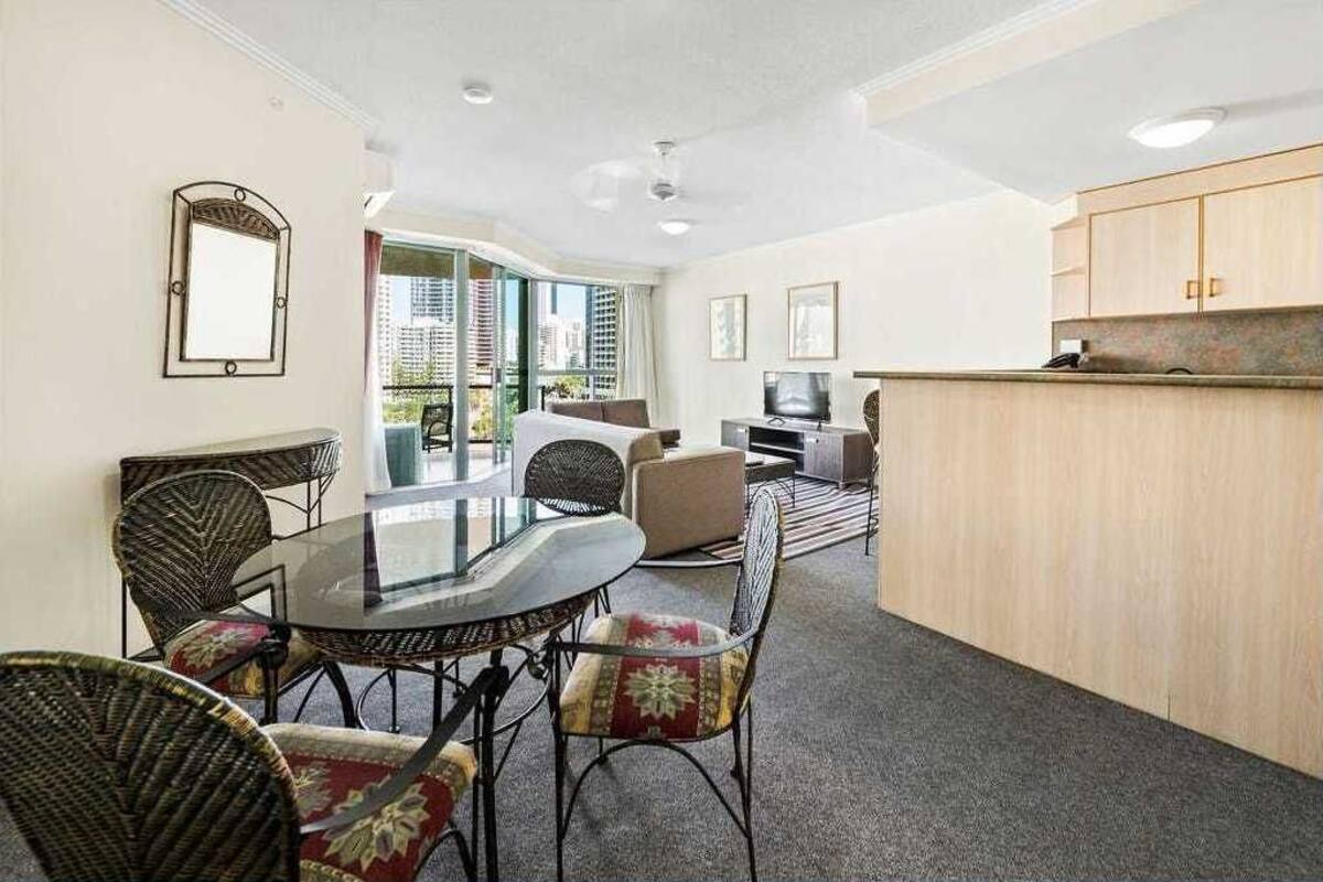 A modern hotel room with a dining area, a sofa, a TV, and a kitchen counter.