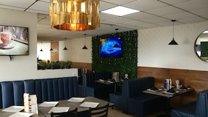 A restaurant interior with booths, tables, and a large TV screen. - Hotel Jatay (Tijuana)