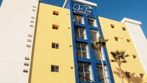 A hotel building with a blue and yellow facade, multiple windows, and palm trees in front. - Hotel Jatay (Tijuana)