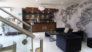 A hotel lobby with a reception desk, a chandelier, a black sofa, and a geometric wall art piece. - Hotel Jatay (Tijuana)