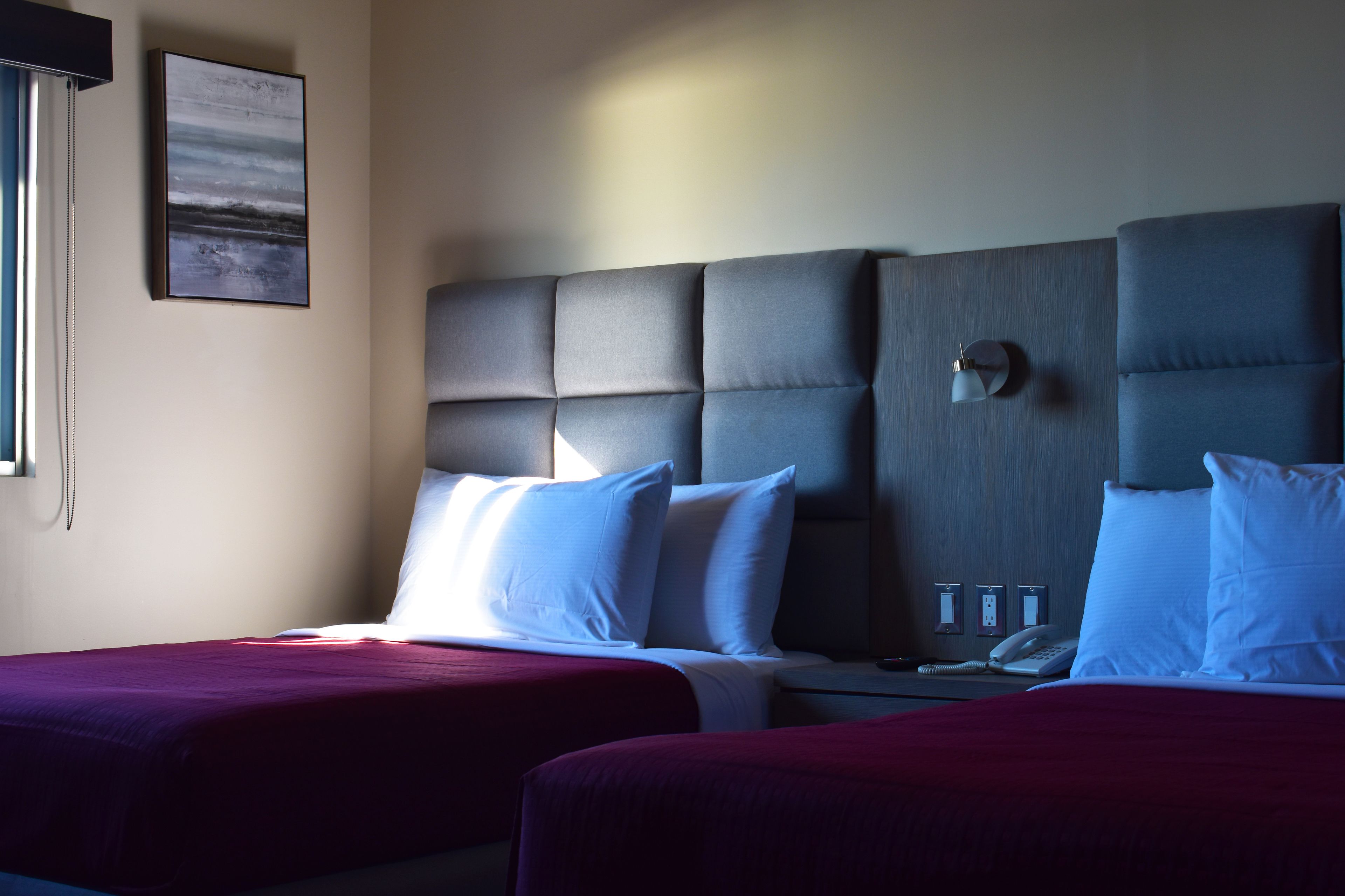 A hotel room with two beds, a headboard, a bedside table with a lamp, and a phone.