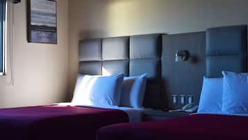 A hotel room with two beds, a headboard, a bedside table with a lamp, and a phone.