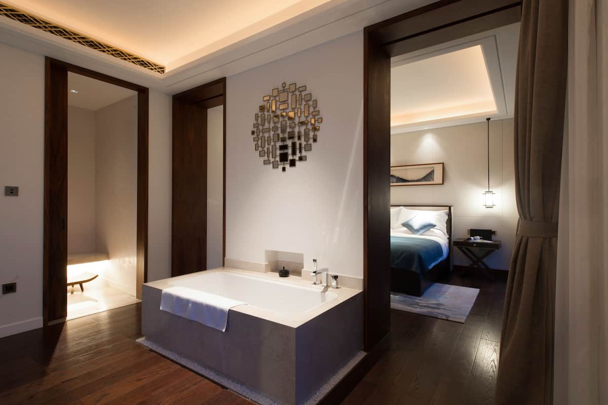 Une salle de bain moderne avec une baignoire sur pieds, un miroir fixé au mur et une table de chevet avec une lampe.