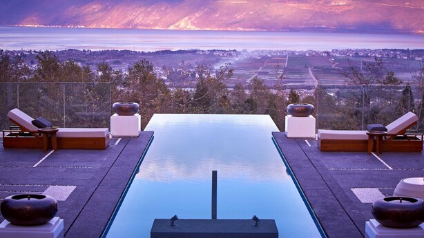 Piscina con sillas de descanso y vistas a una ciudad y montañas.