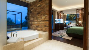 Un baño moderno con una bañera grande, una pared de piedra y vistas al exterior.