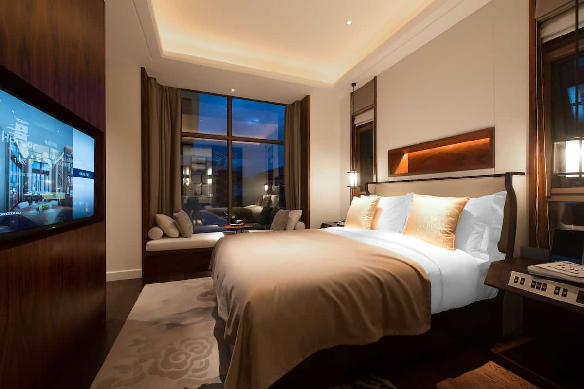Une chambre d’hôtel avec un grand lit, une télévision, un canapé et une fenêtre avec des rideaux.