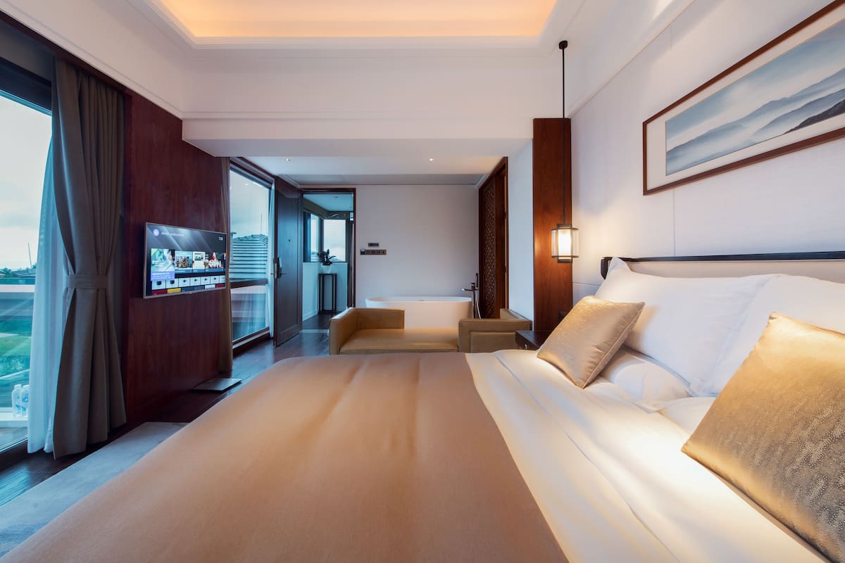 Une chambre d’hôtel moderne dotée d’un grand lit, d’une télévision, d’une baignoire et offrant une vue sur la ville.