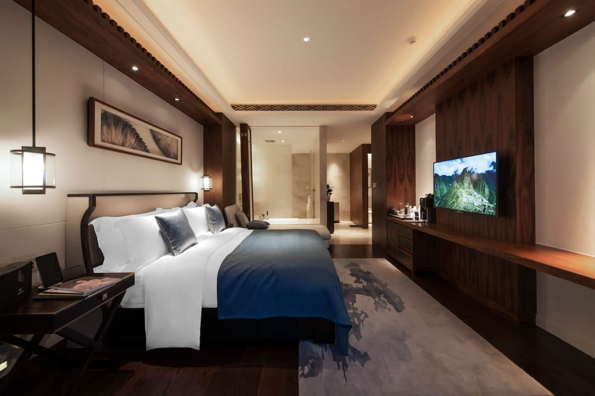 Une chambre d’hôtel moderne équipée d’un grand lit, d’un téléviseur à écran plat, d’un bureau avec un ordinateur portable et d’une table de chevet.